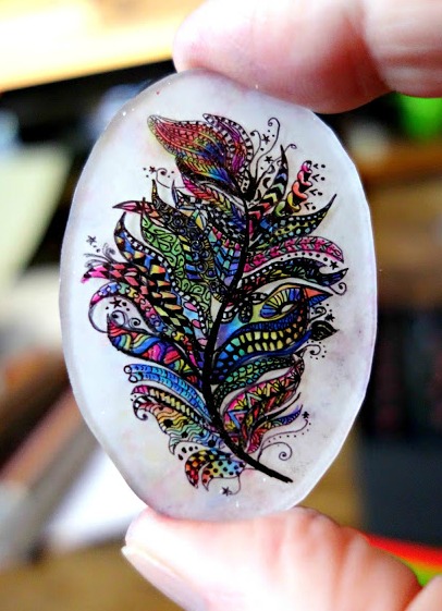 a small piece of shrink plastic with a hand inked rainbow feather