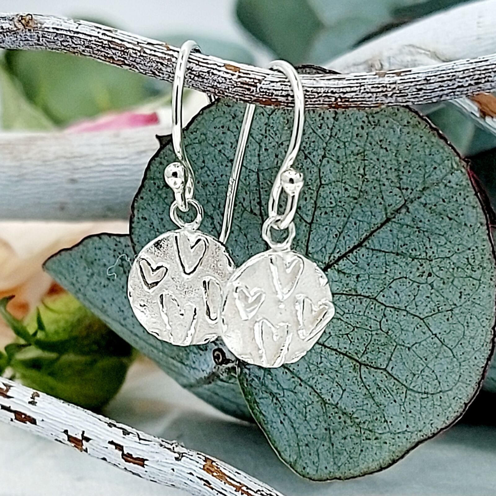 Eye catching handmade silver drop earrings with a subtle raised heart pattern that gently gleams against the frosted matte background.