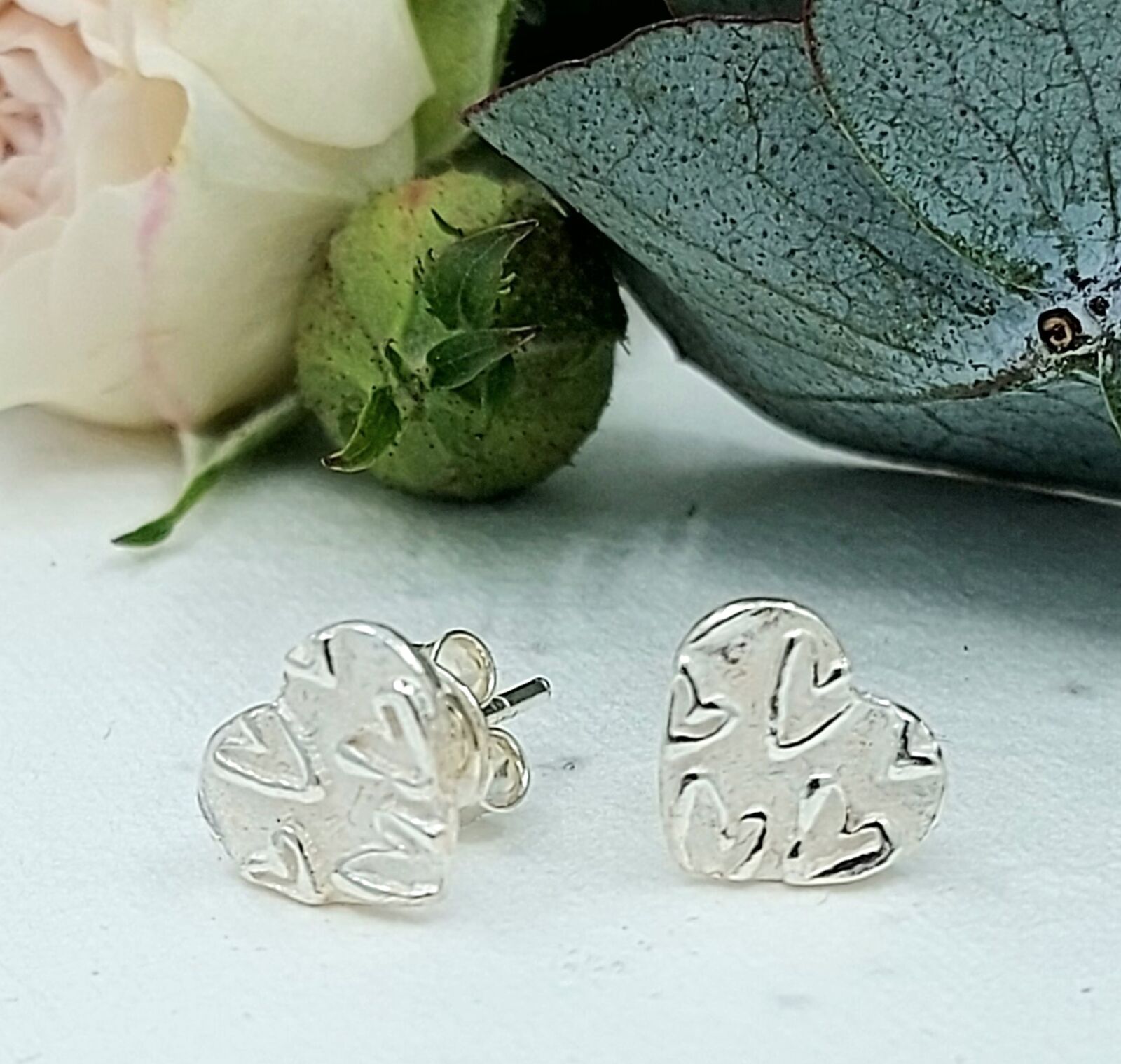 Beautifully handmade silver heart stud earrings with a raised heartdesign, subtly shining against a soft matte background.