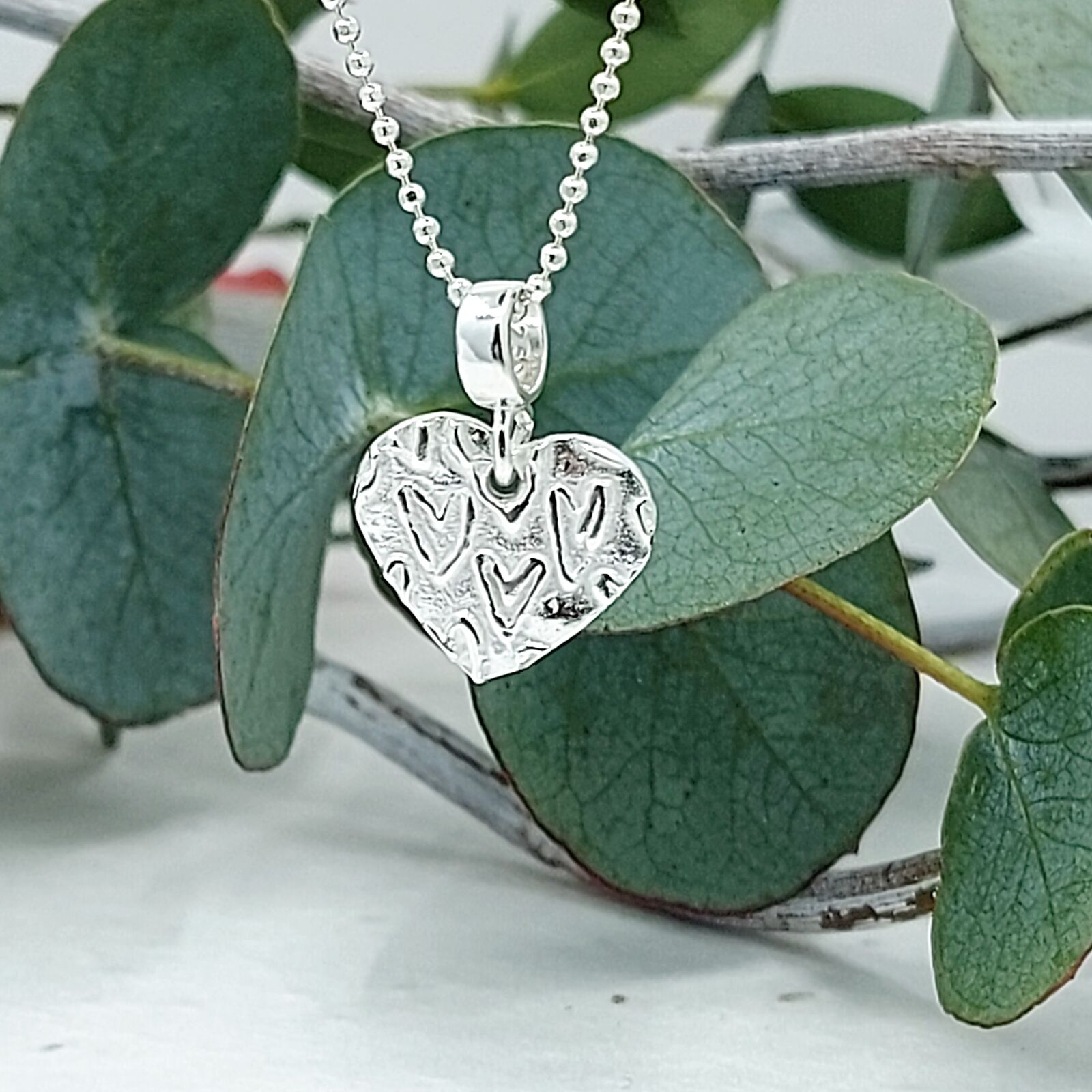 A beautiful artisan heart charm necklace with a soft raised heart pattern that gently gleams against the frosted matte background.