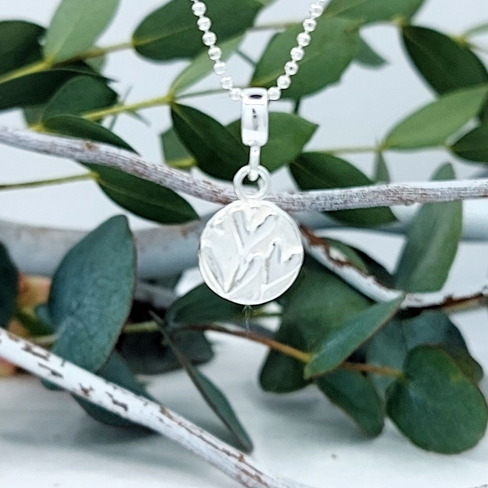 A beautiful artisan silver heart pendant, with a raised heart pattern that subtly gleams against a frosted matte background.